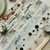A close-up of decorative PET collage tape featuring various markings, lines, and textures on a light background.