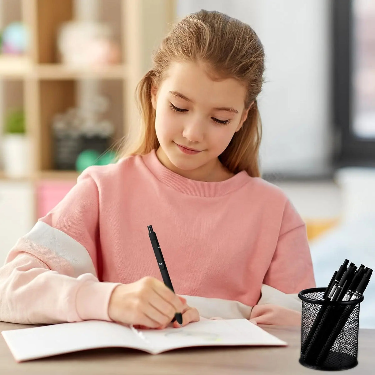 A young girl is writing in a notebook using a set of ten black gel pens and refills.