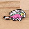 Broche émail avec une créature dinosaurienne rose et jaune et le texte STAY WEIRD