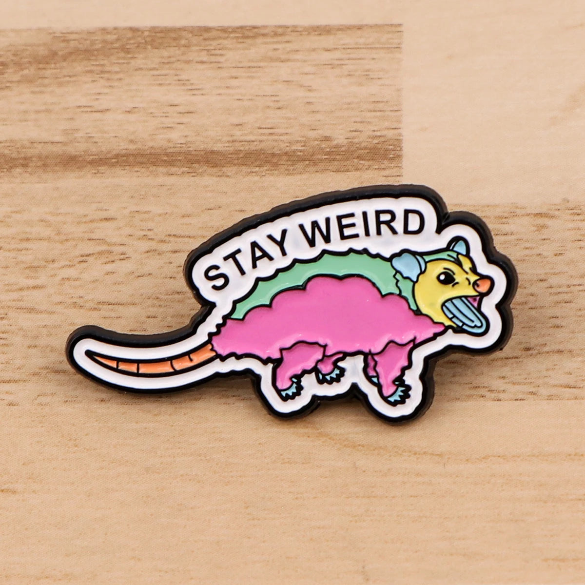 Broche émail avec une créature dinosaurienne rose et jaune et le texte STAY WEIRD
