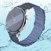A silver-cased watch with a transparent display and a dark gray adjustable magnetic loop band is shown against a watery backg
