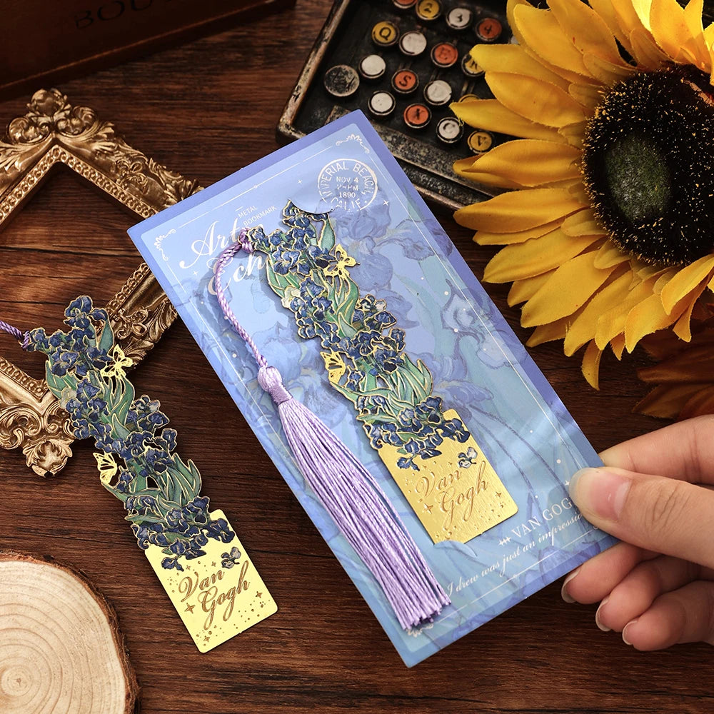 A vintage artistic metal bookmark with a purple tassel is displayed next to a sunflower on a wooden surface.