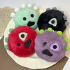 A collection of four plush characters in various colors including green, black, red, and purple arranged on a white plate.