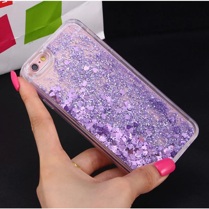 A hand holds a clear glitter purple phone case with heart and star designs against a dark background.