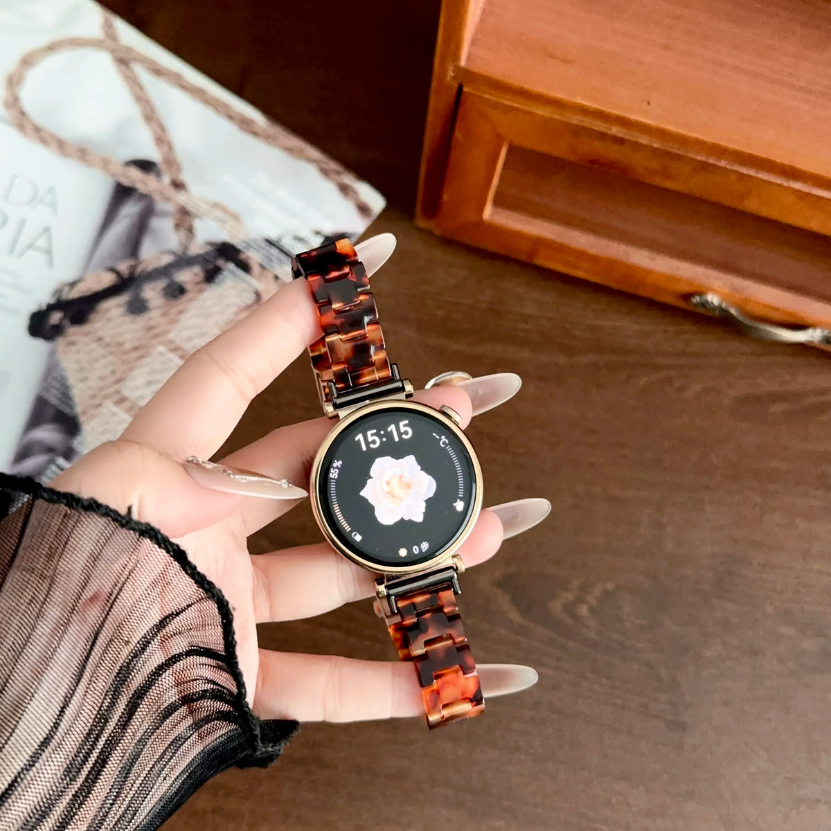 A hand holds an orange resin beaded watch with a white floral design on the face, resting on a wooden surface.