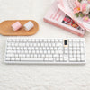 Eine weiße mechanische Tastatur neben rosa Brot und dekorativen Blumen auf weißem Untergrund.