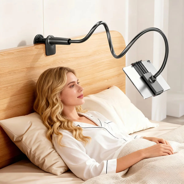 A woman is relaxing in bed with an adjustable tablet and phone holder mounted on the headboard.