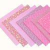 A collection of pink cotton patchwork fabric squares in various patterns including stripes, polka dots, and floral prints for