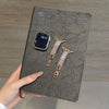 A close-up of a black smartphone and two crystal-embellished gold watch straps resting on a dark gray leather surface.