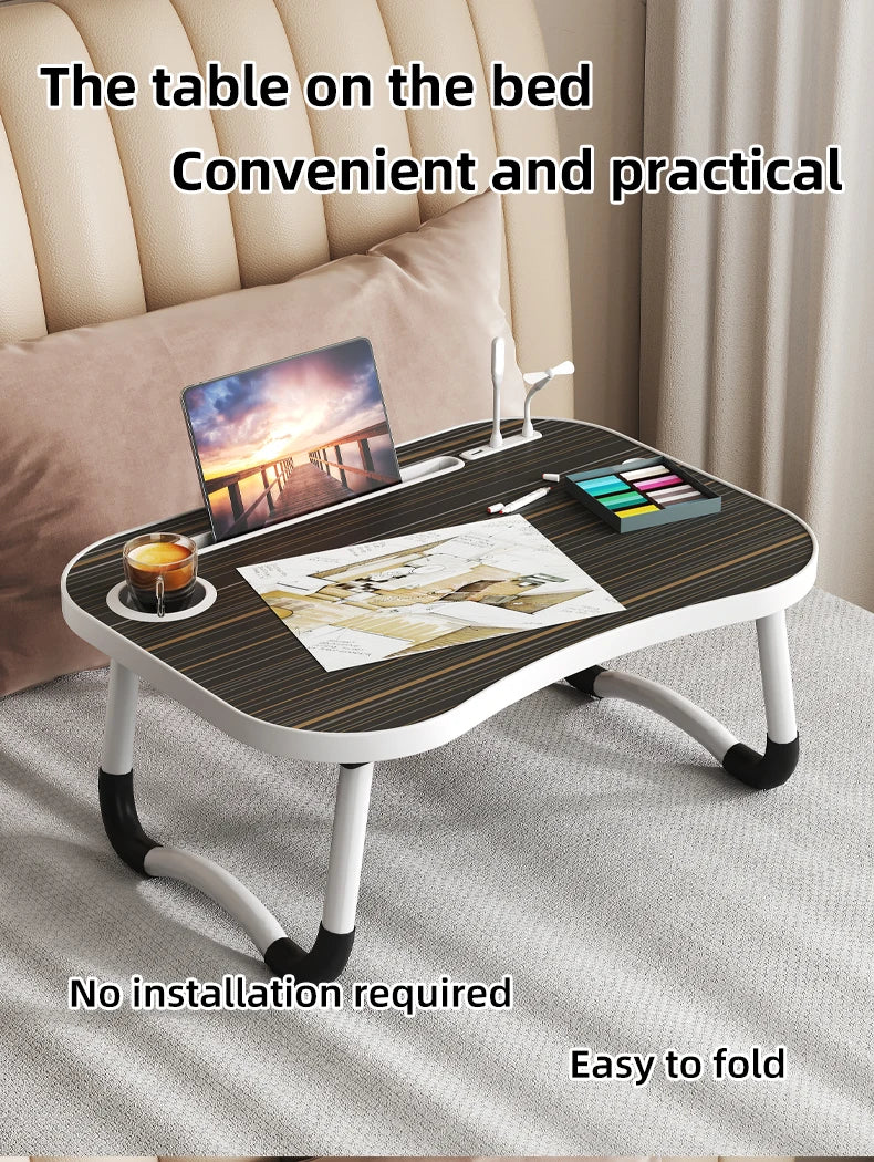 A foldable laptop desk organizer tray with a wooden surface and metal stand placed on a bed.