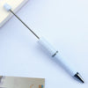 A white DIY beadable pen with a silver clip and black ink tip resting on a light surface.