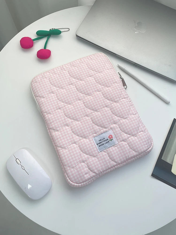 A pink quilted laptop sleeve is shown on a white table next to a silver laptop and a white wireless mouse.