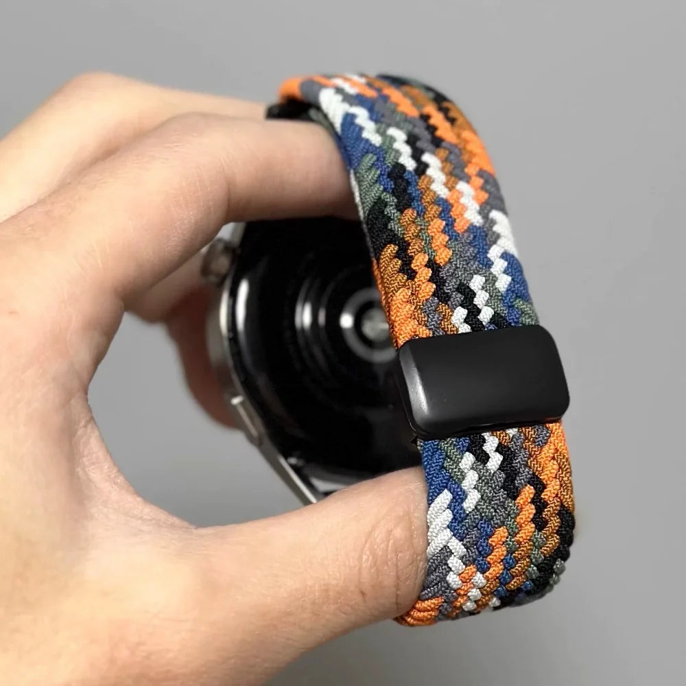 Eine Hand hält ein schwarzes magnetisches Armband mit einem orange-blauen gemusterten Textilriemen.