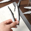 A hand holds a silver and white ocean fish ballpoint pen with a sharp point, resting on a wooden surface.
