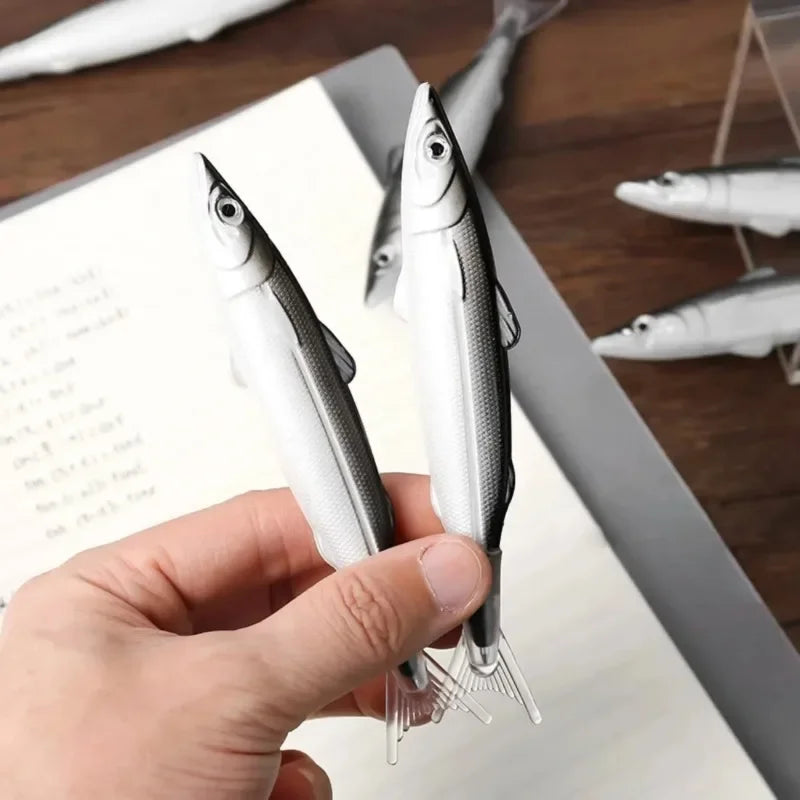 A hand holds a silver and white ocean fish ballpoint pen with a sharp point, resting on a wooden surface.