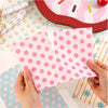 Papel de scrapbook de cuadrícula rosa para diario, mostrado con fondo rojo y varios papeles estampados.