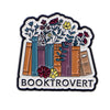 An enamel lapel pin featuring a stylized stack of books with floral elements and the word BOOKTROVERT.