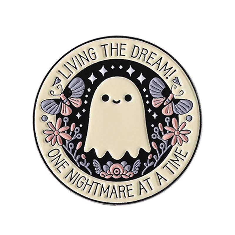 A round enamel pin featuring a white ghost with wings and text that reads Living the Dream One Nightmare at a Time