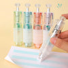 A hand holds a clear double-sided quick dry dot glue pen with four colored tips on a white paper.