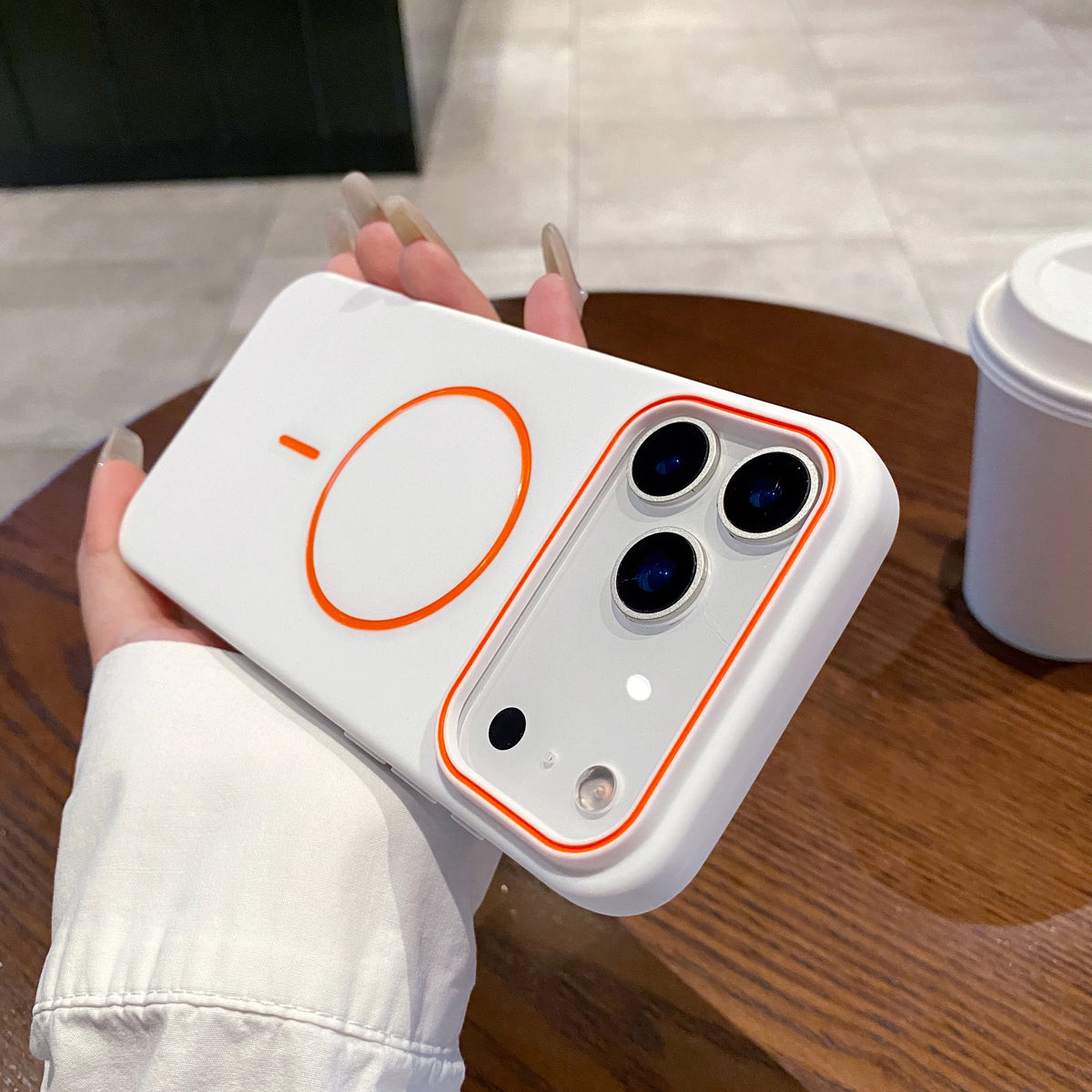 A hand holds a white magnetic wireless charging phone case with an orange circular design on a wooden surface.