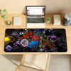 A black mouse pad featuring various cartoon characters and gaming accessories placed on a wooden desk.