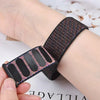 A close-up of a black nylon loop watch strap with pink and blue accents being held by a hand.