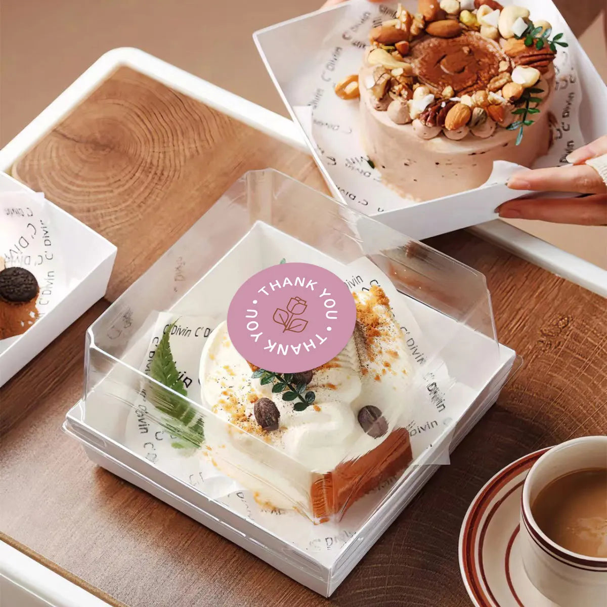 A box of pastel rose thank you stickers roll with a creamy white product displayed on a wooden table.