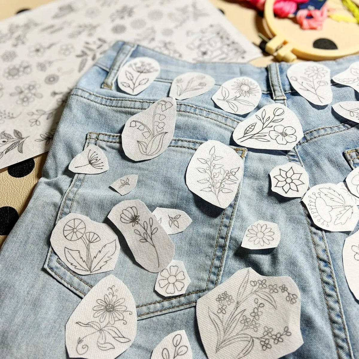 Light wash denim jeans decorated with white embroidery patches featuring floral patterns.