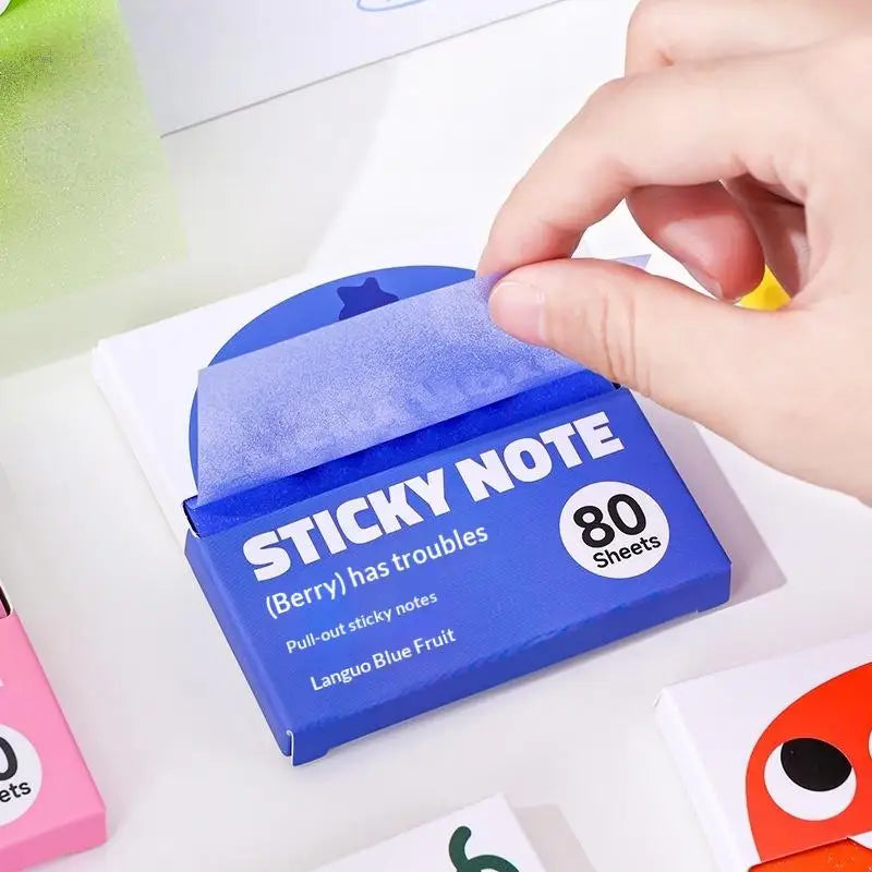 Eine Hand hält eine blaue Box mit Post-its, beschriftet als Sticky Note (Berry), mit Verpackung und Blättern.