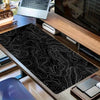 Black and white topographic map extended gaming mouse pad placed on a wooden desk.