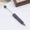 A silver pen accessory with a purple rhinestone bead on the tip and a textured purple body.