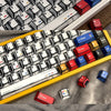 A close-up view of a custom mechanical keyboard with red and blue keycaps resting on a gray fabric surface.