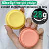 A hand holds two round silicone phone grips, one yellow and one pink, demonstrating a lightweight design.