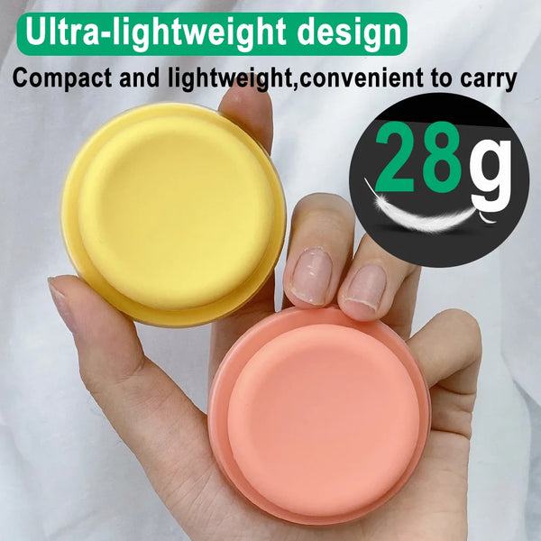 A hand holds two round silicone phone grips, one yellow and one pink, demonstrating a lightweight design.