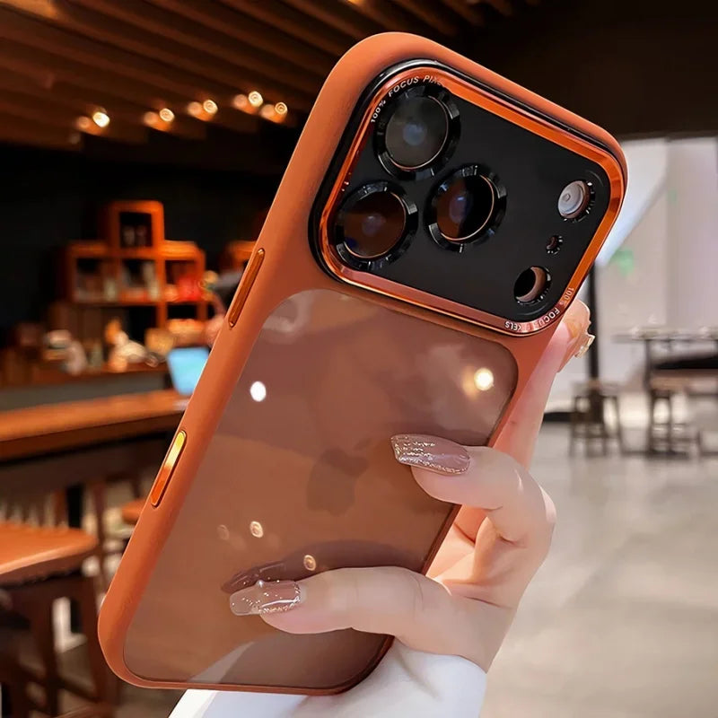 A hand holds an iPhone in a clear shockproof case with camera lens protection, featuring an orange-toned back and gold accent