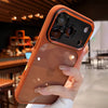 A hand holds an iPhone in a clear shockproof case with camera lens protection, featuring an orange-toned back and gold accent