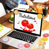 A laptop displaying the word nutritious surrounded by various sliced fruits and vegetables on a wooden table.