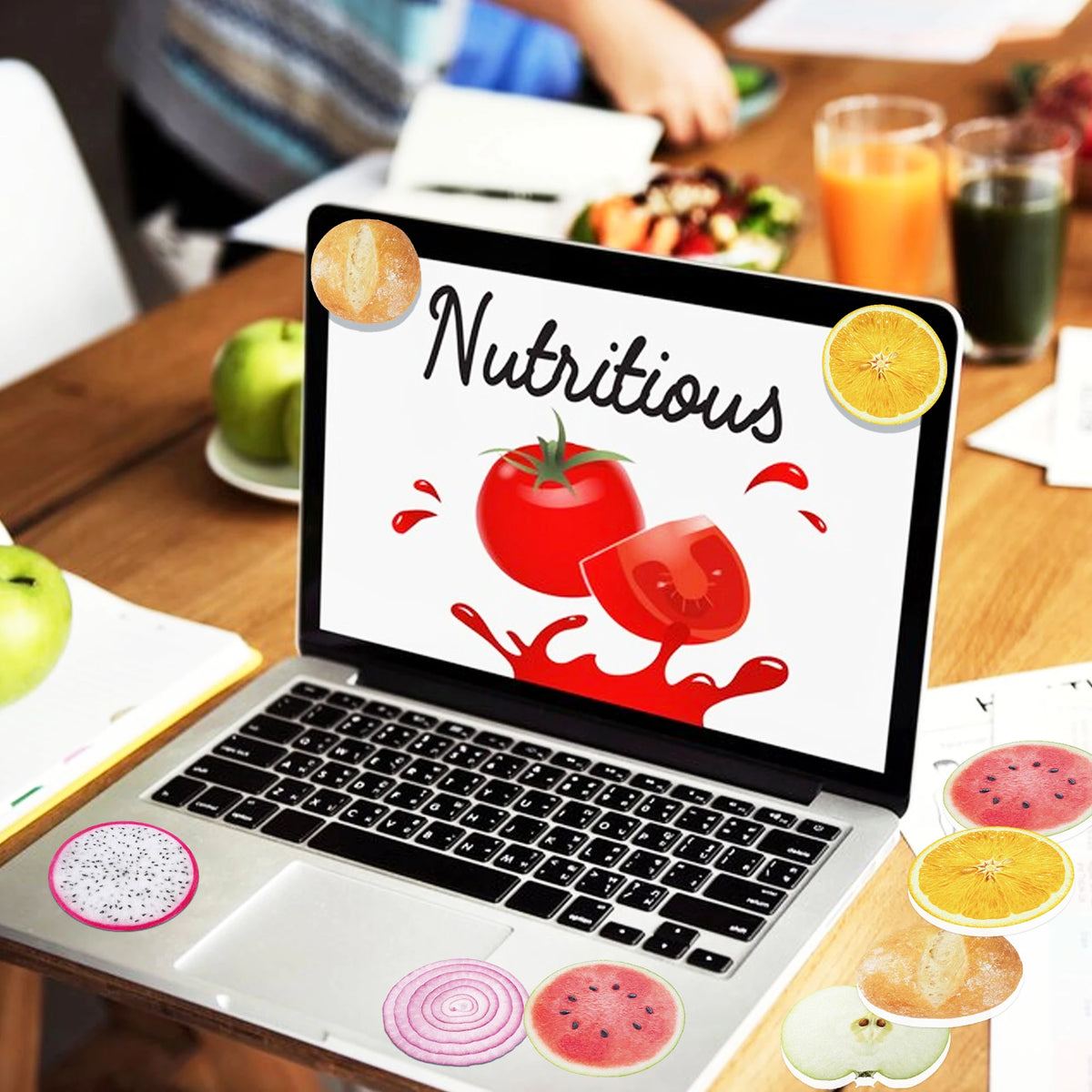 A laptop displaying the word nutritious surrounded by various sliced fruits and vegetables on a wooden table.