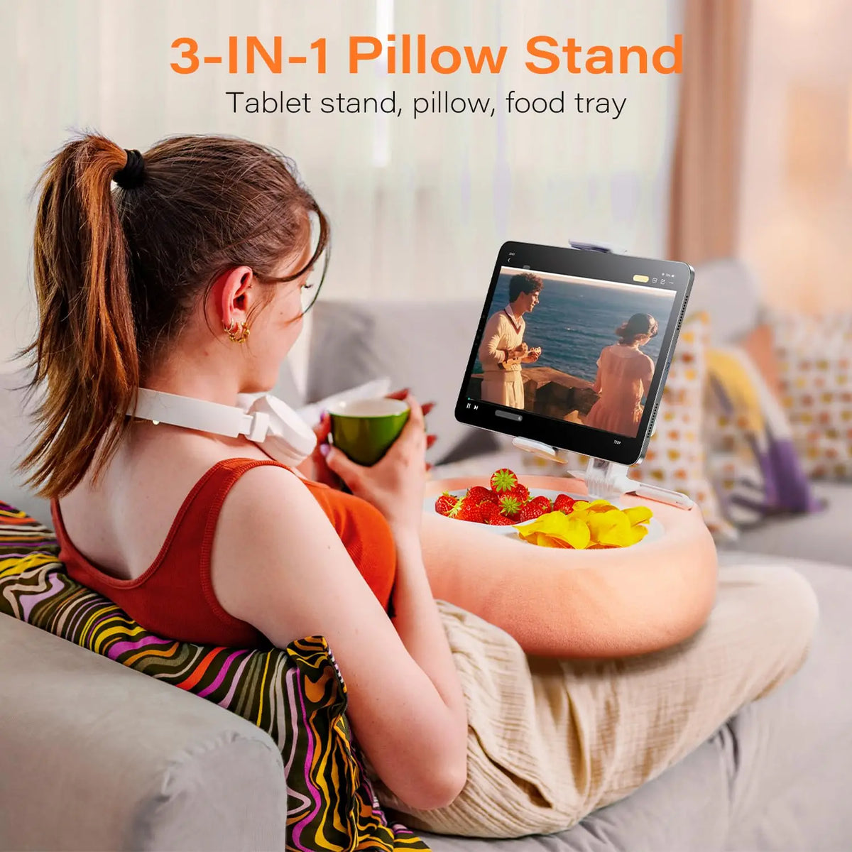 A woman is using a 3-in-1 pillow stand to hold a tablet, pillow, and food tray while relaxing on a couch.