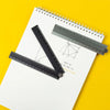 A precision aluminum folding ruler is shown on a white sheet of paper against a yellow background.