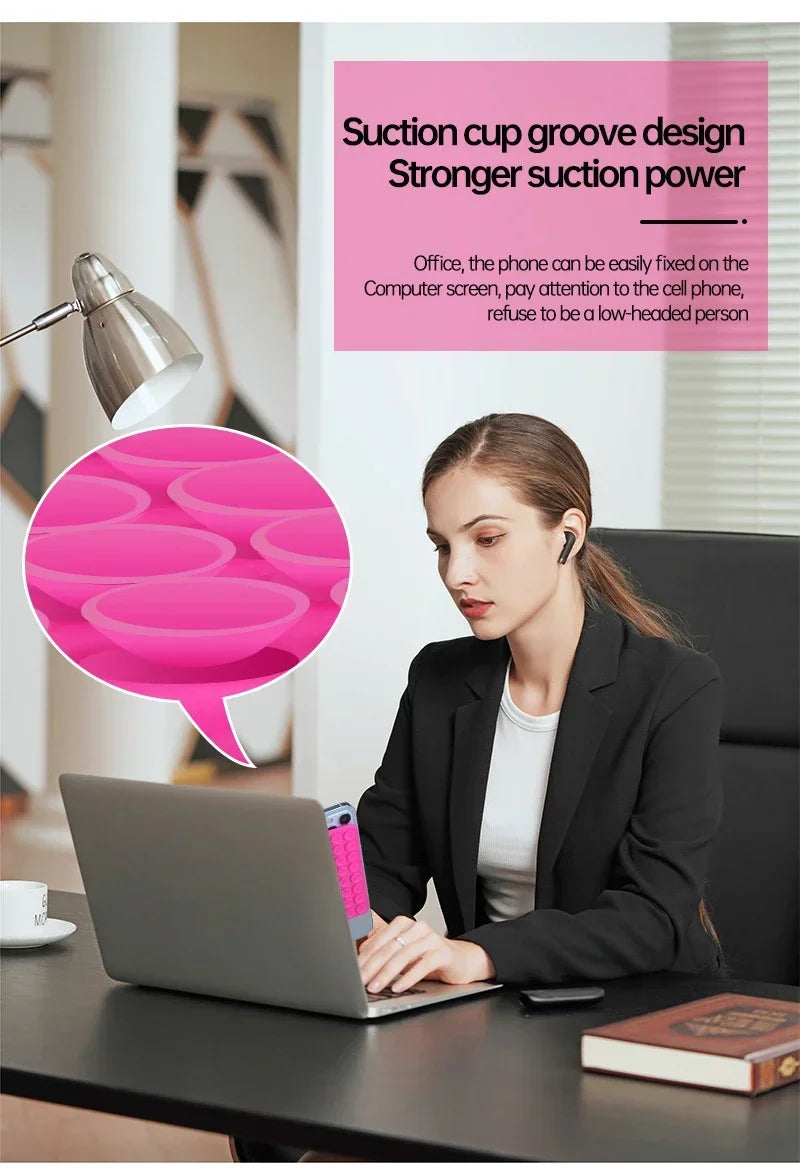 A woman is using a silicone suction cup phone holder on a laptop in an office setting.