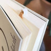 A close-up of a cream-colored book with a gold bookmark ribbon inserted, showing the title page.