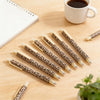 A set of leopard print retractable ballpoint pens lying on a wooden surface next to a cup of coffee.
