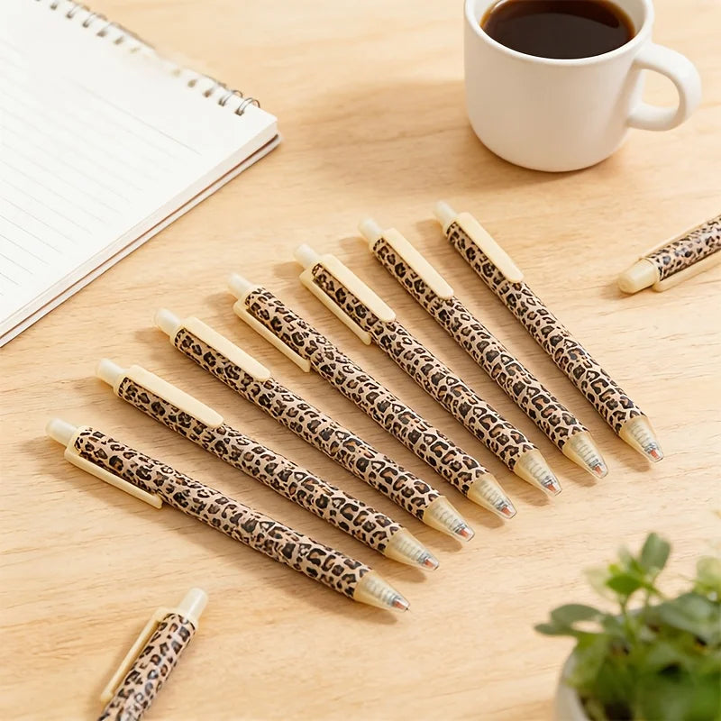 A set of leopard print retractable ballpoint pens lying on a wooden surface next to a cup of coffee.