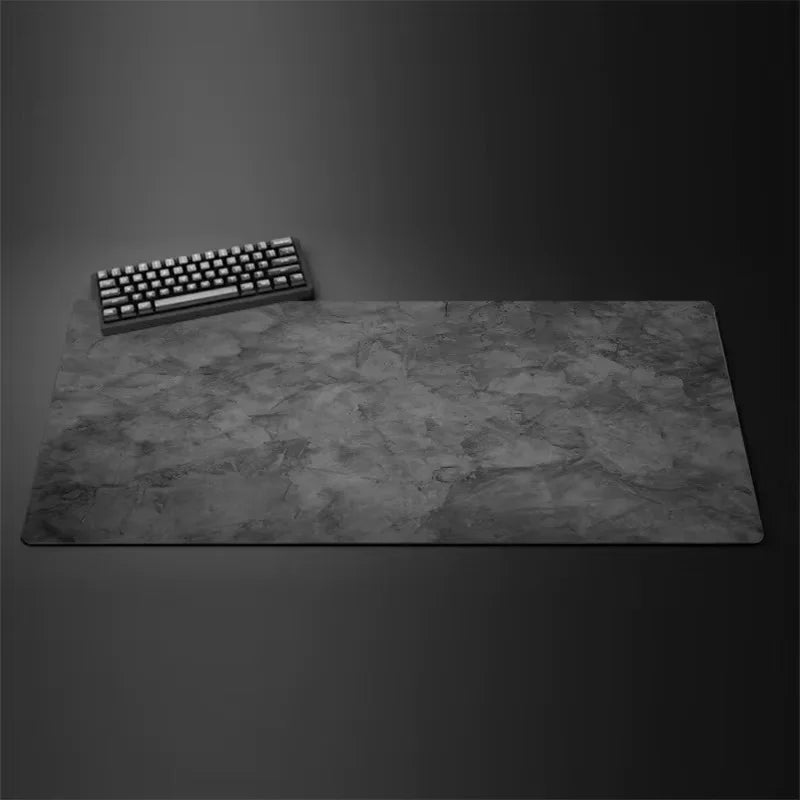 A gray overlocked mouse pad is placed on a dark surface next to a computer keyboard.