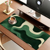 A dark green mouse pad with beige wavy patterns placed on a wooden desk next to a laptop.