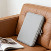 A gray waterproof PU leather laptop sleeve resting on a brown leather sofa next to an open magazine.