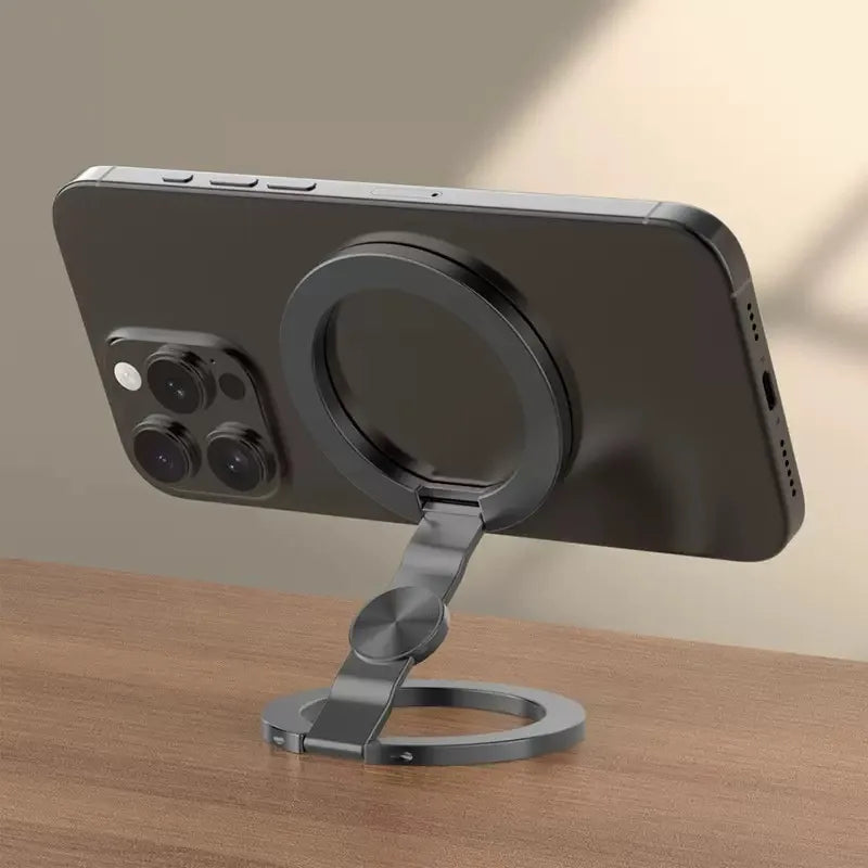 A dark gray foldable dual-sided phone stand with MagSafe compatibility resting on a wooden surface.