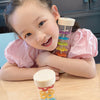 A young girl holds a wooden rain sound tube musical instrument filled with colorful beads and a wooden stopper.