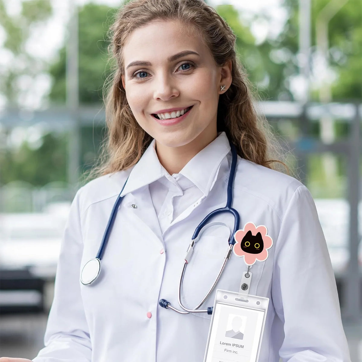 A smiling woman in a white lab coat wearing a stethoscope and holding an ID badge holder.